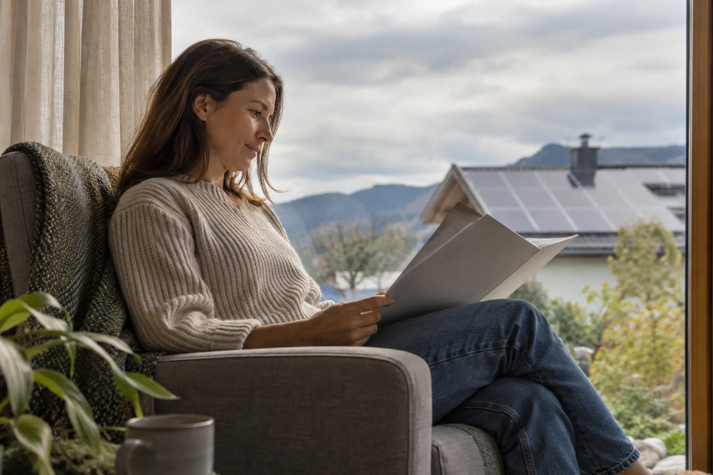 Person liest unbeschriftete Unterlagen an einem Fenster mit Blick auf ein Solardach